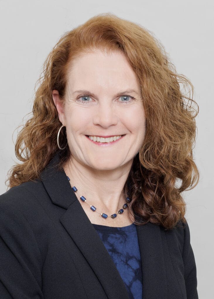 A woman with long red hair wearing a black jacket.